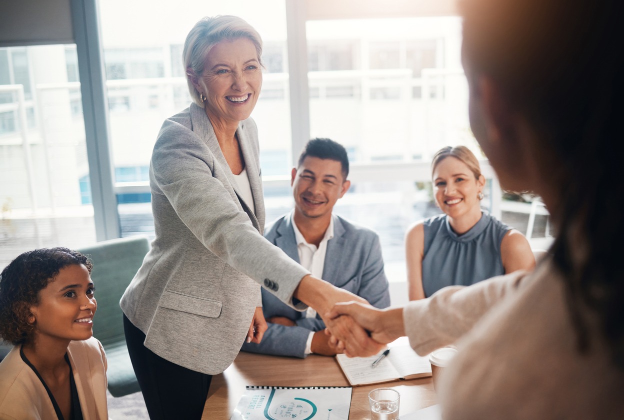 Group of 4 in business attire in conference room. One person is shaking hands with someone out of shot.
