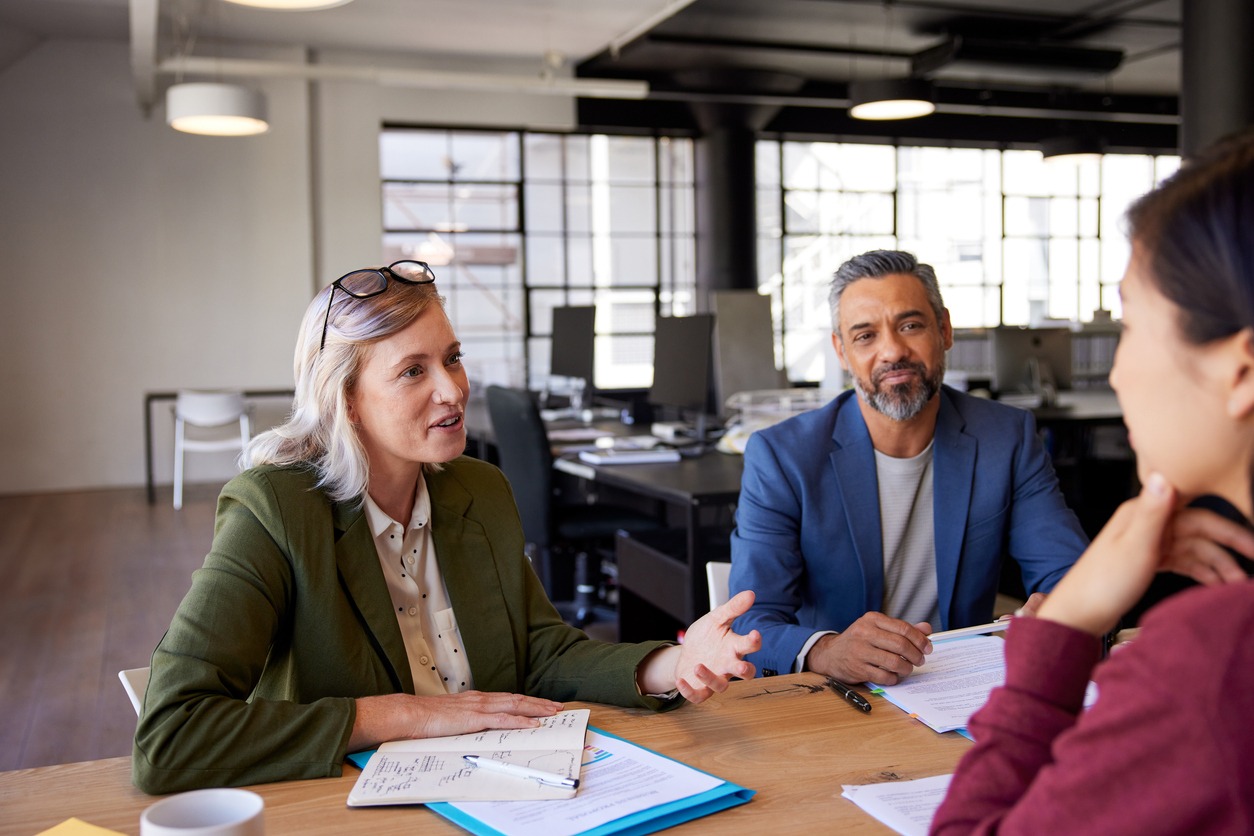 1 woman and 1 man are interviewing a woman at a table in an empty office