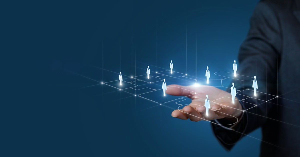 A hand holding up a graphic of a process flowchart showing silhouettes of people standing in different areas.