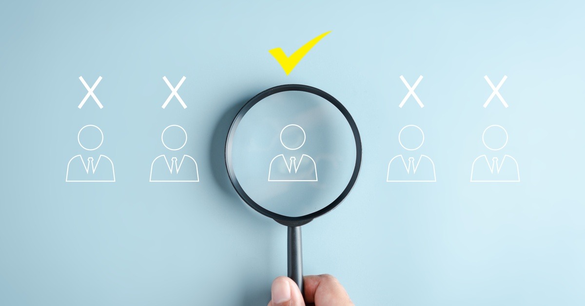 A hand holds a magnifying glass over a doodle of a person with a yellow checkmark above their head, between 4 similar doodles.
